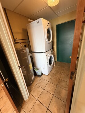 A laundry room with stacked washers and dryers, a water heater, and a green door.