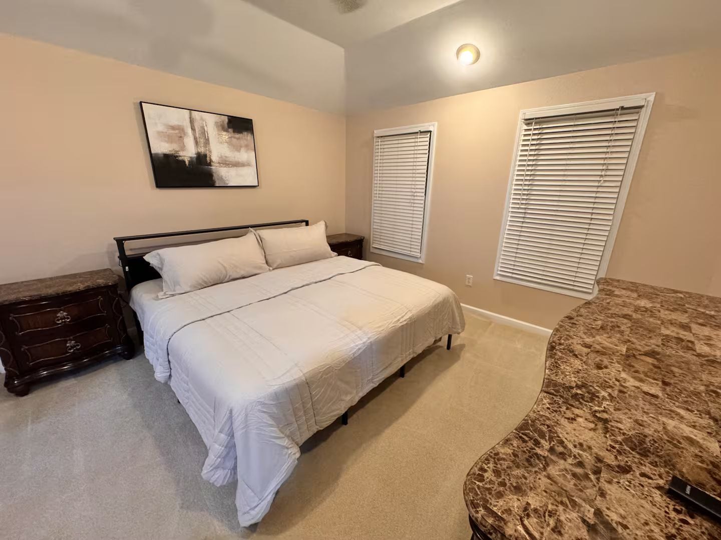 Een slaapkamer met een bed, een dressoir, een schilderij en twee ramen met zonwering.