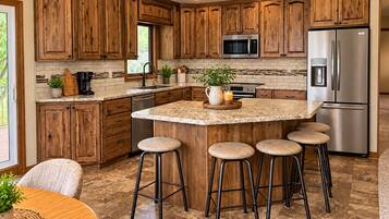 A kitchen with wooden cabinets, a stainless steel refrigerator, a microwave, and a central island with stools.