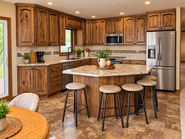 A kitchen with wooden cabinets, a stainless steel refrigerator, a microwave, and a central island with stools.