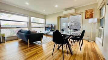 Uma sala de estar moderna com área de jantar, janelas amplas e parede de destaque em tijolo.