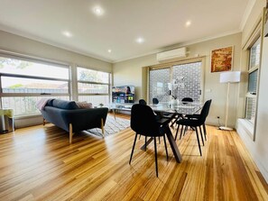 Uma sala de estar moderna com área de jantar, janelas amplas e parede de destaque em tijolo.