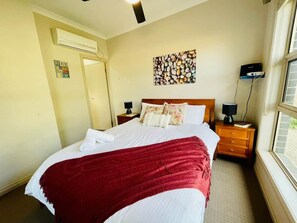 Quarto de hotel com cama, mesa de cabeceira, luminária, ar-condicionado, obra de arte na parede e janela com vista.