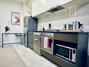 A modern kitchen with stainless steel appliances, a built-in oven, and a microwave. - Stylish High-Rise City Retreat near Southern Cross (Melbourne)