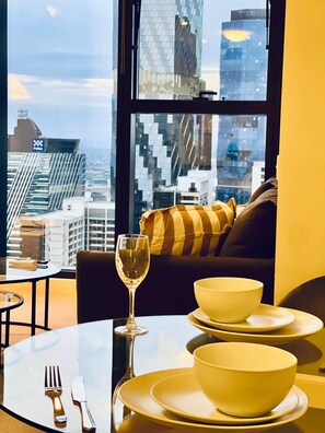 A dining area with a table set for two, a wine glass, and a bowl on a plate. - Stylish High-Rise City Retreat near Southern Cross (Melbourne)