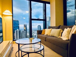 A modern living room with a large window, a sofa, and a glass coffee table. - Stylish High-Rise City Retreat near Southern Cross (Melbourne)