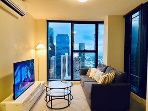 A modern living room with a large flat-screen TV, a glass coffee table, and a sofa with cushions. - Stylish High-Rise City Retreat near Southern Cross (Melbourne)