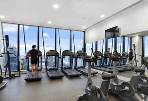 A gym with treadmills and exercise equipment, large windows with a city view, and a ceiling with recessed lighting. - Stylish High-Rise City Retreat near Southern Cross (Melbourne)