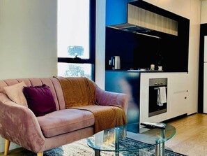 A modern living room with a sofa, a glass coffee table, and a kitchen area with a stove and cabinets. - Stunning Stay Steps away from Crown w/Free Parking (Southbank)