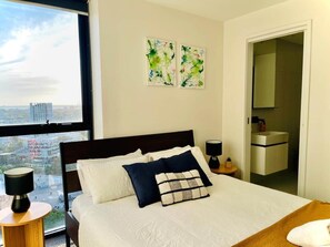 Een hotelkamer met een groot bed, twee nachtkastjes, een raam met uitzicht op de stad en een deur naar een badkamer.