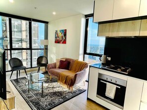 A modern kitchen with a stove, oven, and a large window. There is a sofa and a coffee table in the living area. - Stunning Stay Steps away from Crown w/Free Parking (Southbank)