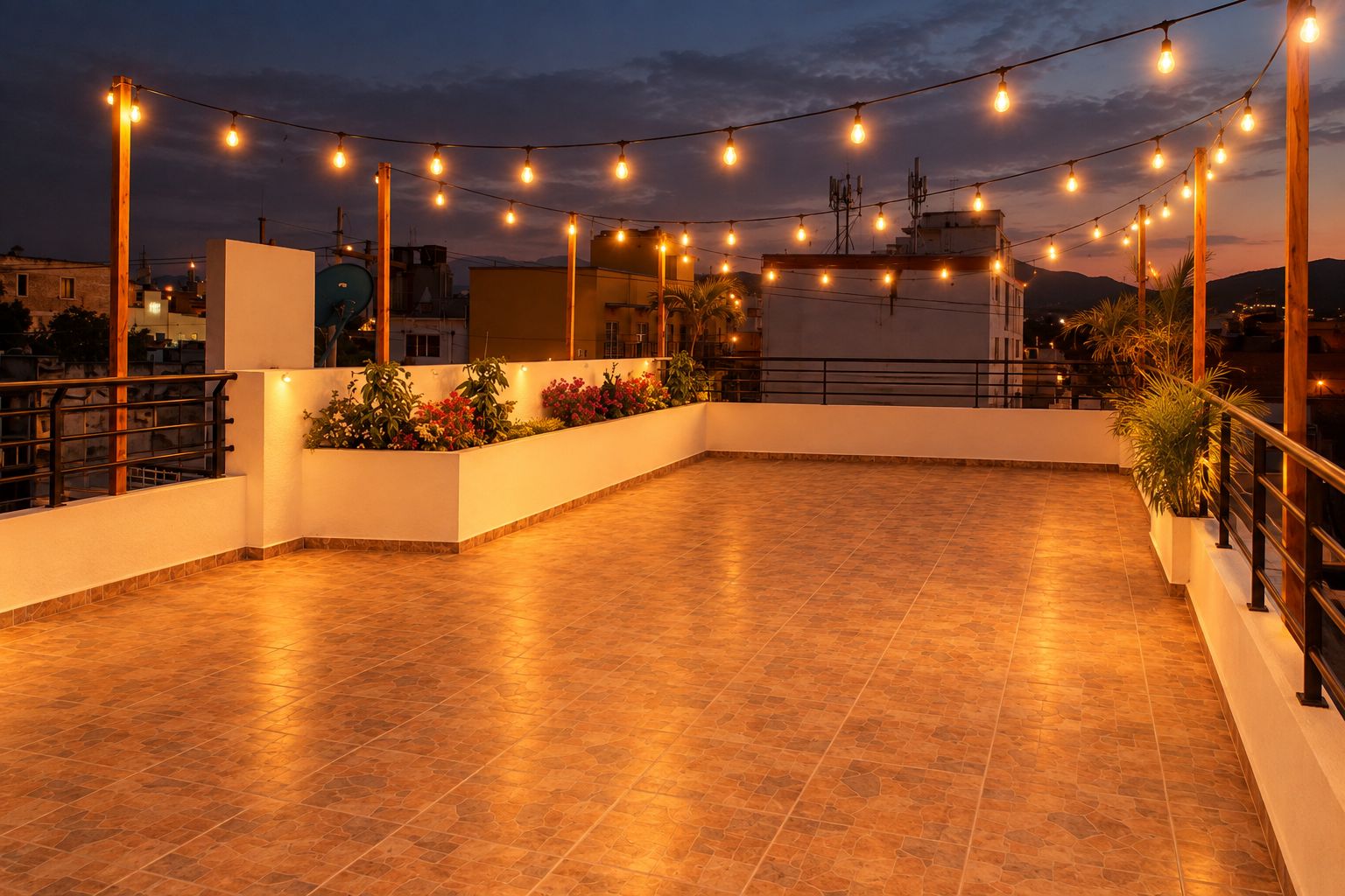 An outdoor terrace with a tiled floor, surrounded by plants and a railing, under string lights.