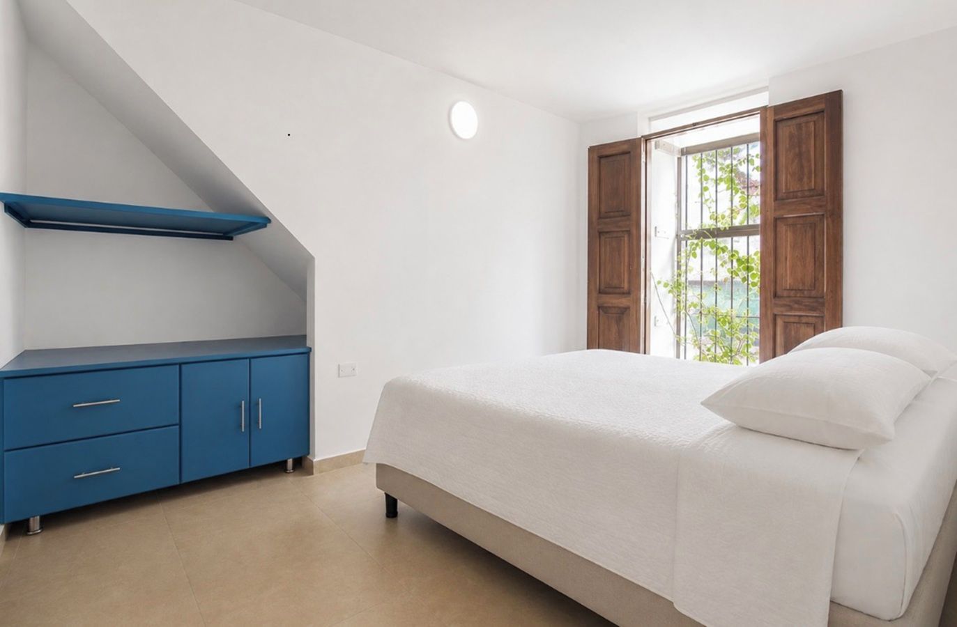 Ein Schlafzimmer mit einem Bett, einer blauen Kommode und einem Fenster mit Blick.