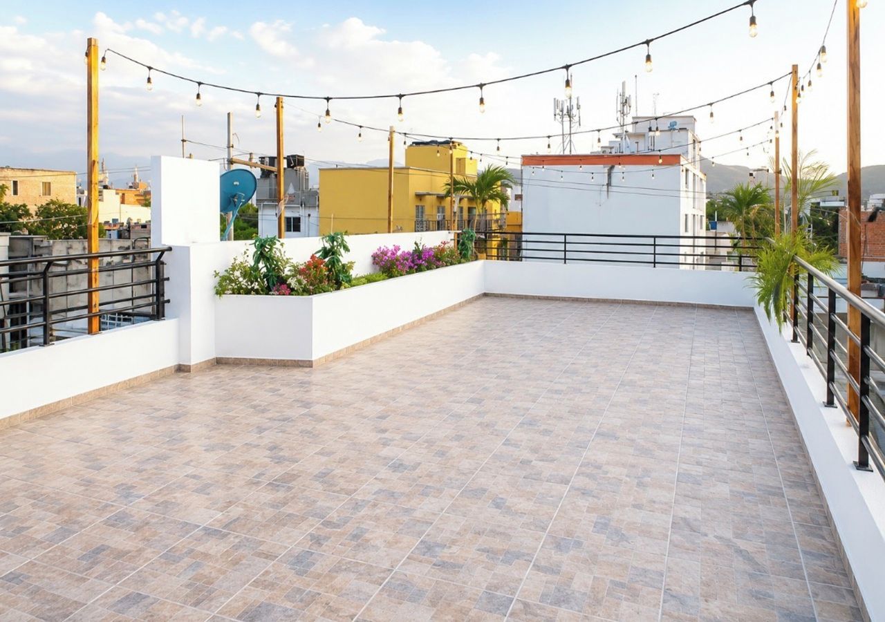 A rooftop terrace with a tiled floor, a white wall with a black railing, and string lights.