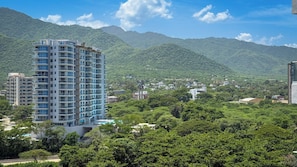 A high-rise building with multiple balconies, surrounded by lush greenery and mountains in the background. - Spacious, modern studio apartment 80 meters from Bello Horizonte Beach with an ocean view (Unknown)