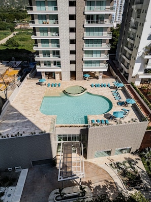 A rooftop swimming pool with sun loungers and a small hot tub, surrounded by a high-rise building. - Spacious, modern studio apartment 80 meters from Bello Horizonte Beach with an ocean view (Unknown)