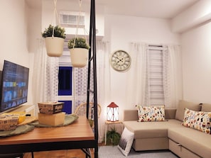 A cozy living room with a wooden table, a sofa, a wall clock, and a television.