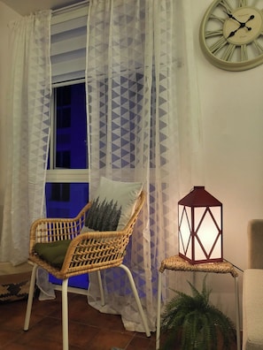 A room with a wicker chair, a wall clock, a lantern, and a window with a geometric curtain. - Cozy La Bella Tagaytay Stay Pool View + Work Space (Tagaytay City)