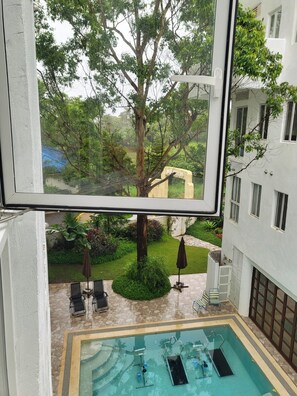 A view from a window of a swimming pool area with lounge chairs and a tree.