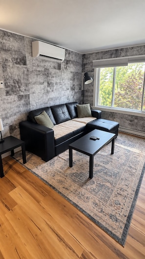 A modern living room with a sectional sofa, a coffee table, and a large window with a view of trees. - Vintage & lumineux • Secteur calme (Montréal)