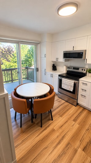 A kitchen with a round table and chairs, a microwave, stove, and cabinets. - Vintage & lumineux • Secteur calme (Montréal)