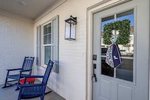 A white brick exterior with a gray door, two blue chairs, a lantern, and a wreath with a bag hanging on the door. - Rebel Retreat - Close to the Square, Campus and MTrade Park! (Oxford)