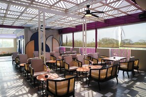 An indoor seating area with tables and chairs, a ceiling fan, and large windows. - Mansionite Hotel Kudus (Kudus)