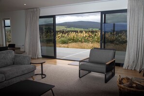 Una sala de estar moderna con un gran ventanal corredera que da a un balcón con vistas a un campo y colinas.