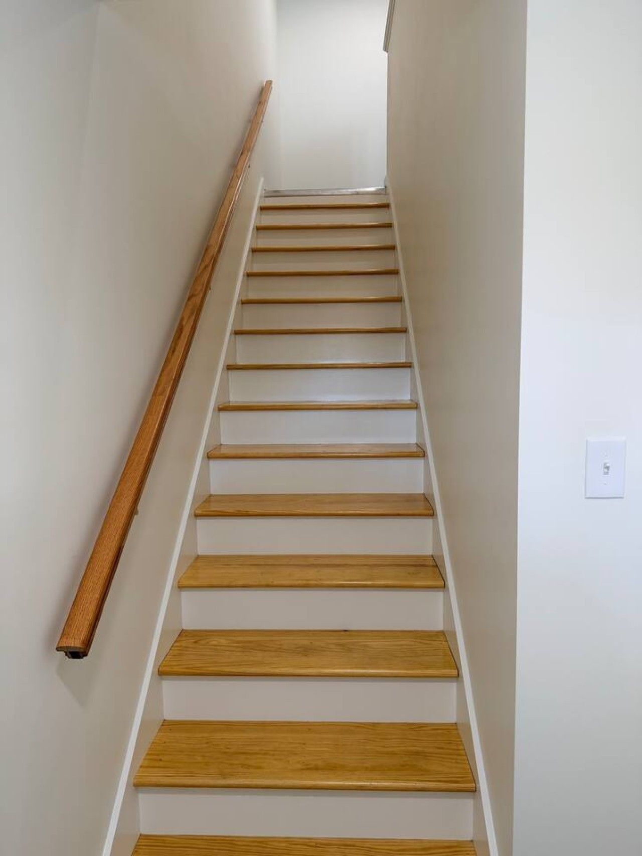 A staircase with wooden steps and a handrail on the left.