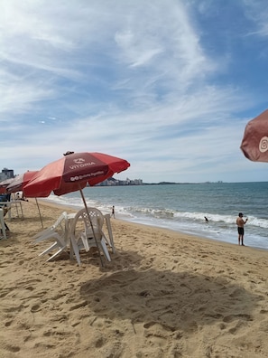 A beach with umbrellas and chairs, a view of the sea, and a distant city skyline.
