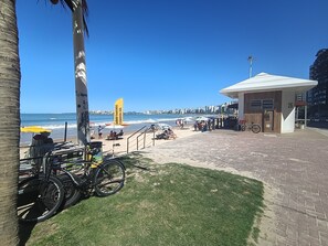 Vista de la playa con un paseo pavimentado, bicicletas y sombrillas.