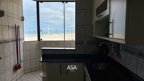 A kitchen with a window overlooking a beach, a sink, and a countertop. - ASA Pe na Areia 3QT Beto Carrero Gravata (Navegantes)