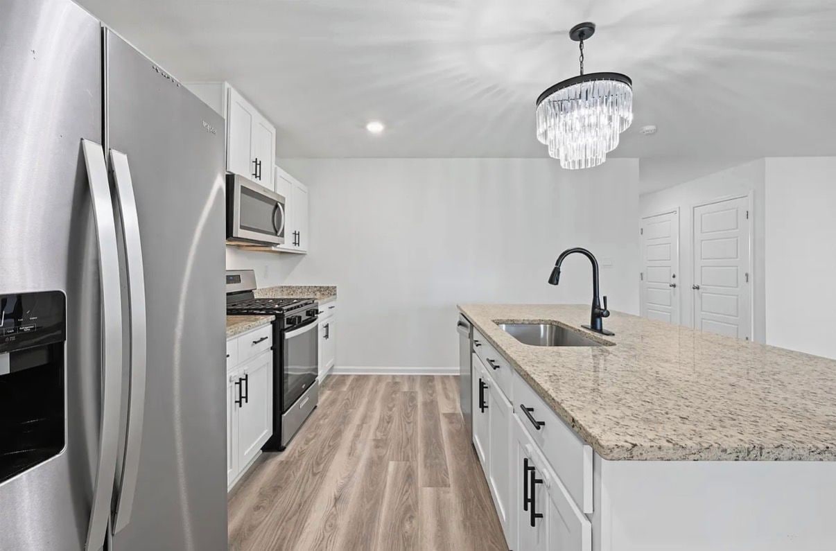 A modern kitchen with stainless steel appliances, a granite countertop, and a chandelier.