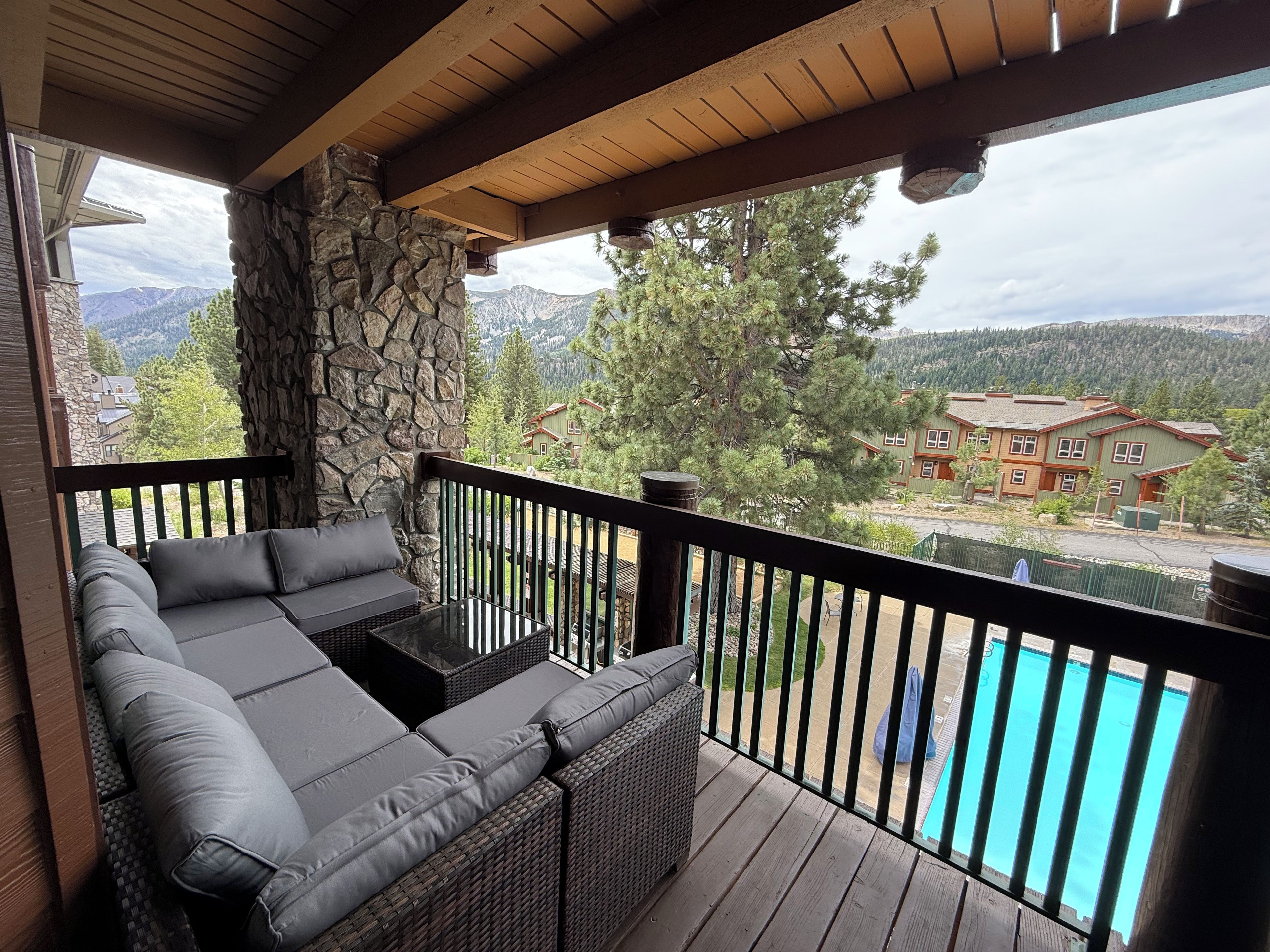 A covered outdoor seating area with a stone pillar, a pool, and a view of a mountain and residential buildings.