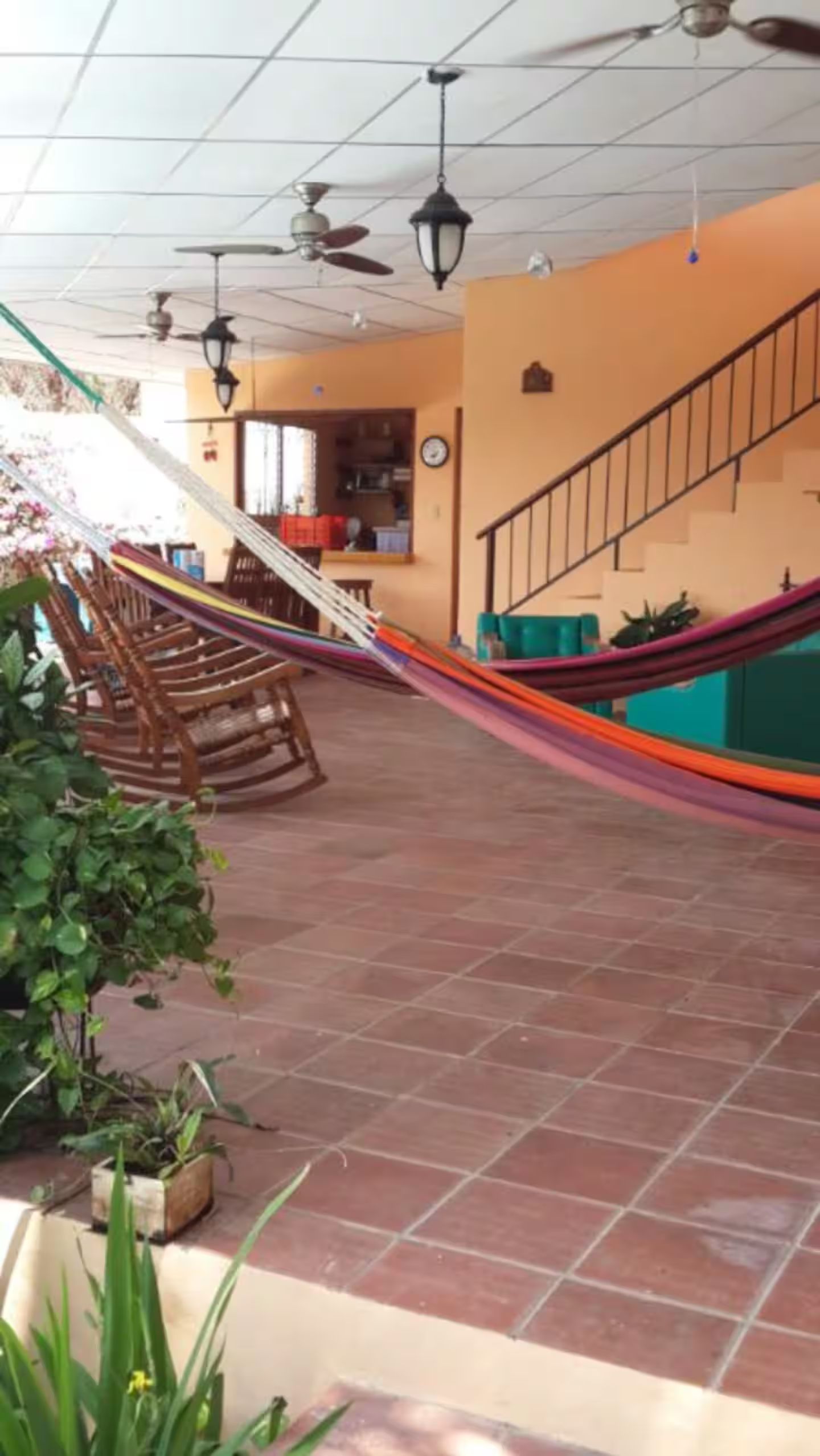 A spacious indoor area with a tiled floor, a hammock, ceiling fans, and a staircase.