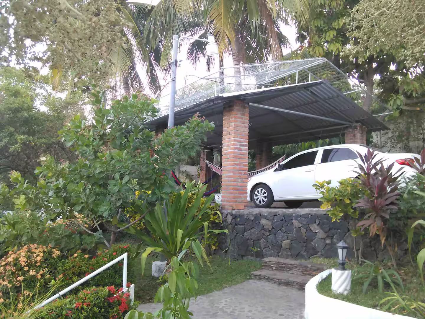 A white car parked under a covered area with a stone wall and greenery.