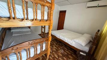A room with a bunk bed, a single bed, a ceiling fan, an air conditioning unit, and a wooden floor.