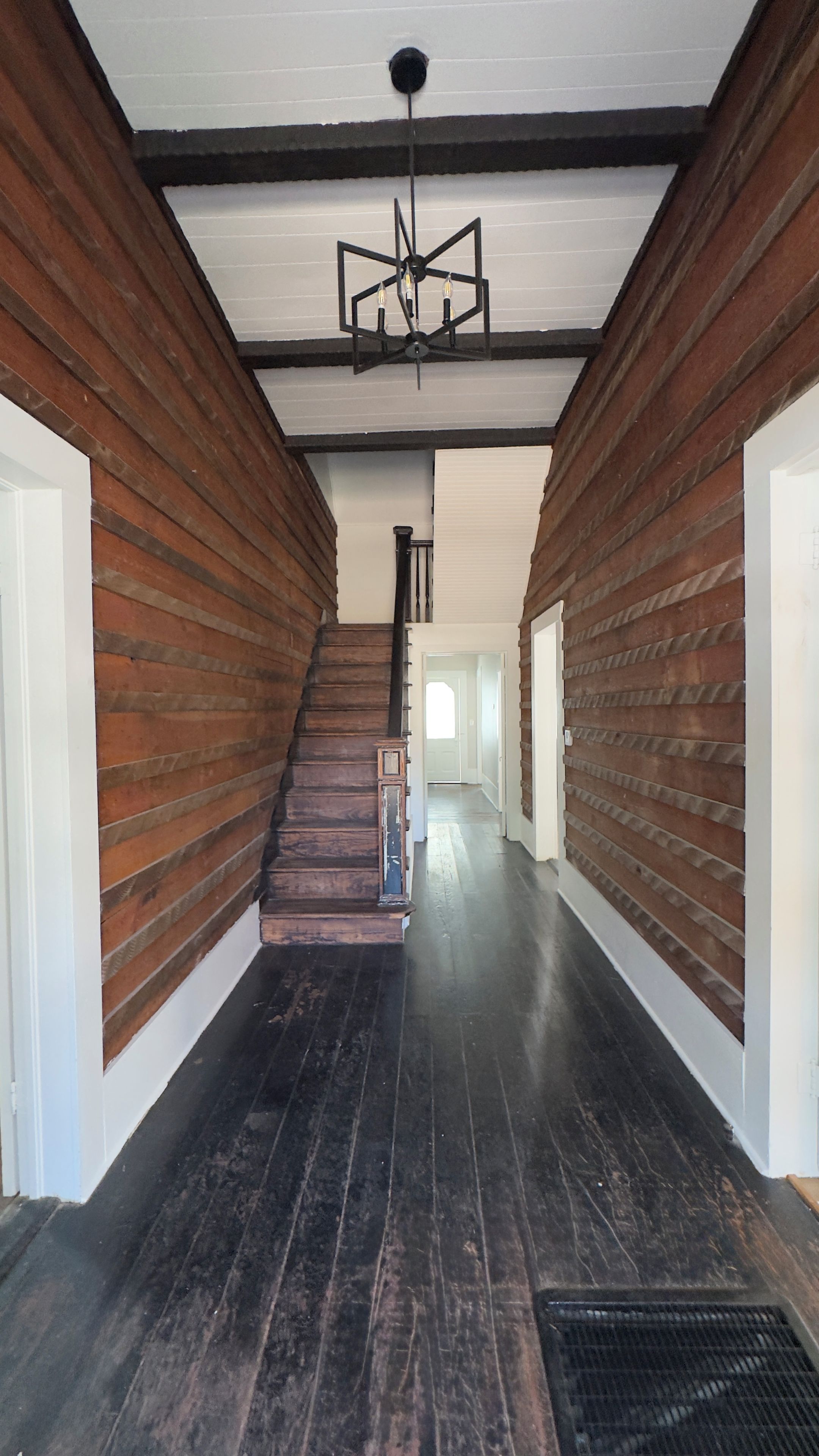 Un pasillo con paneles de madera, una escalera y una lámpara moderna.