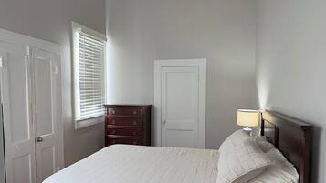 A bedroom with a bed, a ceiling fan, a dresser, a nightstand, and a window with blinds.