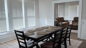 A dining area with a ceiling fan, a dining table set for six, and a view of the living room through an open doorway.