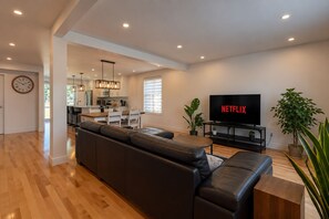 A modern living room with a leather sofa, a flat-screen TV, and a dining area in the background. - Spacious and Modern, Close to Metro and Amenities (Montréal)