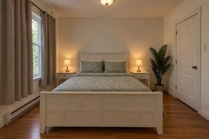 A bedroom with a bed, two bedside tables, a nightstand, a potted plant, and a door. - Spacious and Modern, Close to Metro and Amenities (Montréal)