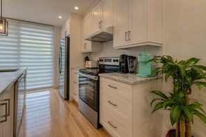 A modern kitchen with white cabinets, stainless steel appliances, and a countertop with a coffee maker and plant. - Spacious and Modern, Close to Metro and Amenities (Montréal)