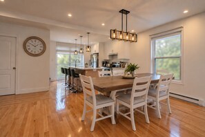 A modern kitchen with a central island, white cabinetry, and a dining area with a wooden table and white chairs. - Spacious and Modern, Close to Metro and Amenities (Montréal)