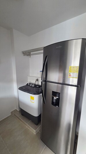 Ein Edelstahl-Kühlschrank mit Wasserspender, einer Mülltonne und einer Steckdose an der Wand.