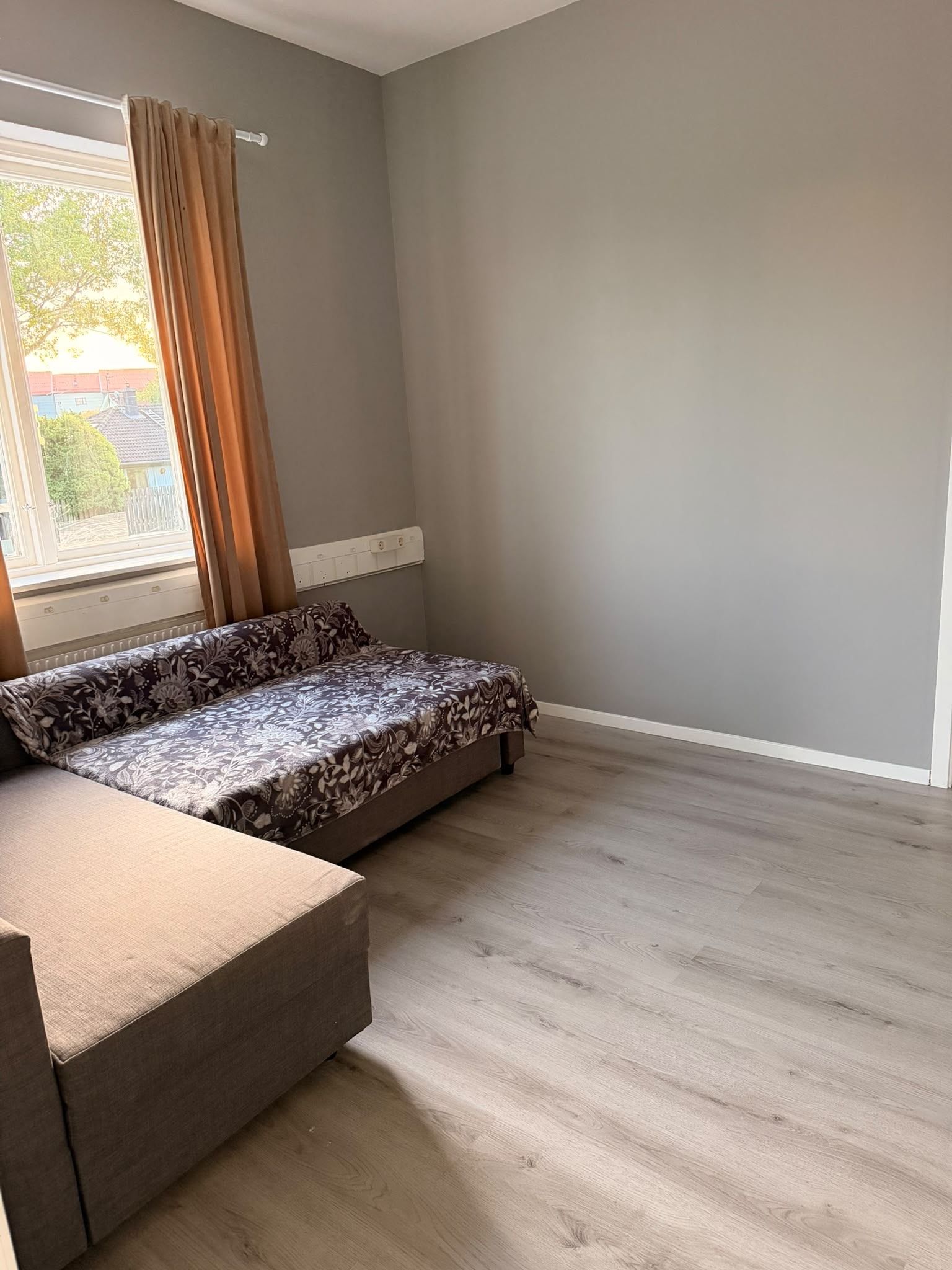 A room with a bed, a sofa, a window with curtains, and a radiator.