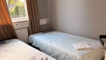 Habitación con dos camas individuales, cada una con una colcha de estampado de leopardo, un radiador y una ventana con cortinas.