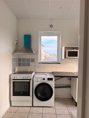 Una cuina compacta amb forn Bosch, rentadora, microones i finestra amb vista a edificis.