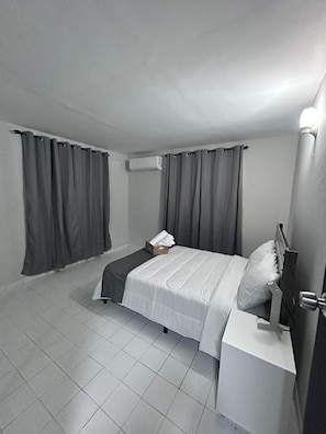 A bedroom with a bed, curtains, an air conditioning unit, a bedside table, and a nightstand. - Nice and accessible apartment in San Juan area, very walkable distance to malls. (San Juan)