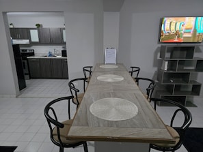 A modern dining area with a long wooden table, black chairs, and a television mounted on the wall. - Nice and accessible apartment in San Juan area, very walkable distance to malls. (San Juan)
